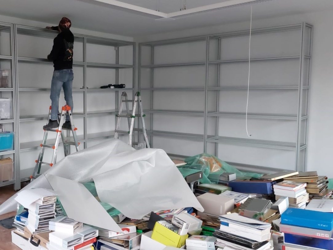 Installation phase of the Oltrefrontiera Material Library showing the aluminium shelving system during setup